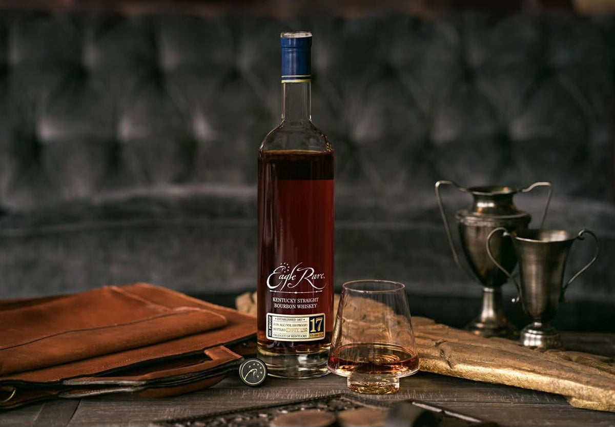 Eagle Rare 17 Year bourbon with a glass on a wooden table beside silver trophies