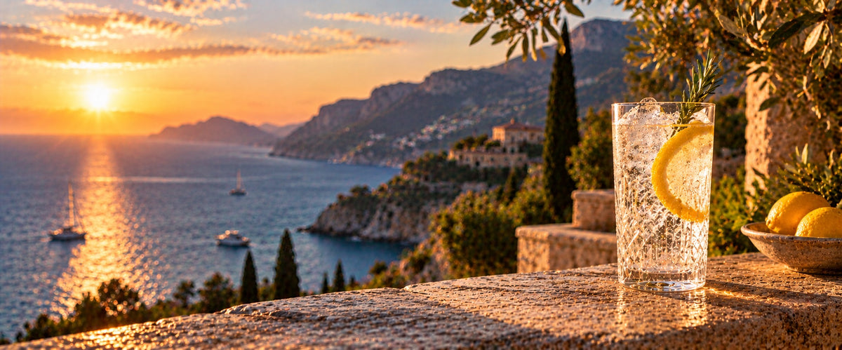 Gin and tonic with lemon and rosemary on a stone wall above the Mediterranean coast at sunset